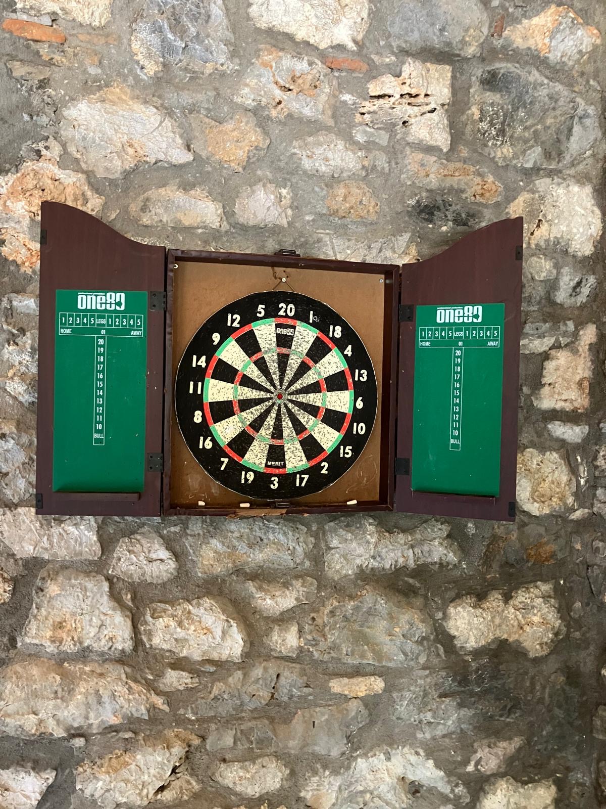 Darts in the pool house Dartboard mounted in a wooden cabinet on the stone wall of the Villa Arcadia game room
