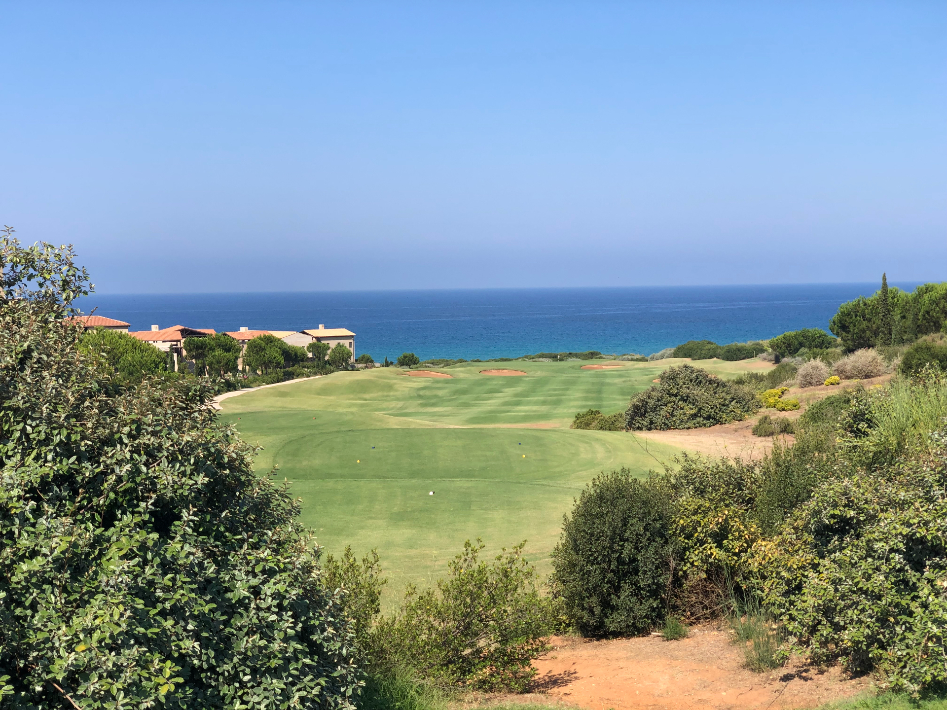 A clifftop fairway at Costa Navarino with the Ionian Sea beyond Costa Navarino fairway running down to the Ionian Sea with cliffside resort buildings